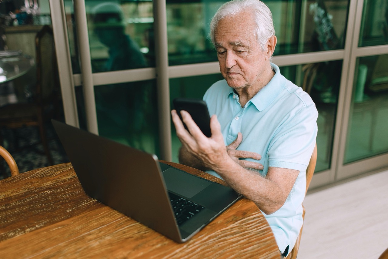 Senior nimmt per Smartphone und Laptop an einem curendo Pflegekurs teil