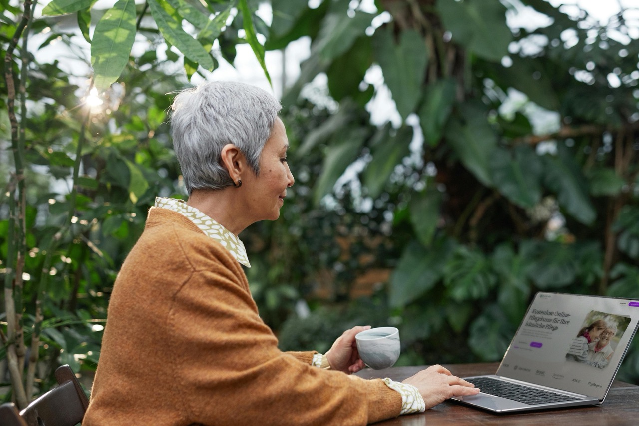Seniorin nutzt curendo Online-Pflegekurse auf dem Laptop im Garten