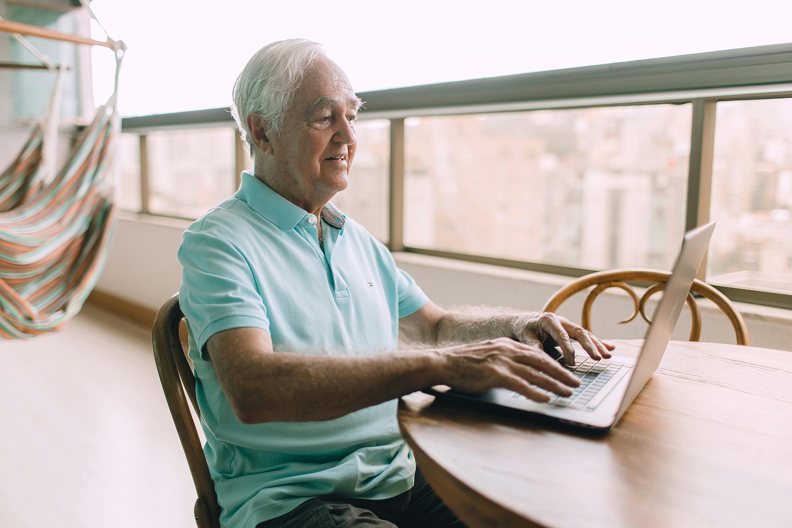Älterer Mann sitzt auf dem Balkon und startet einen Online-Pflegekurs zur häuslichen Pflege auf dem Laptop.
