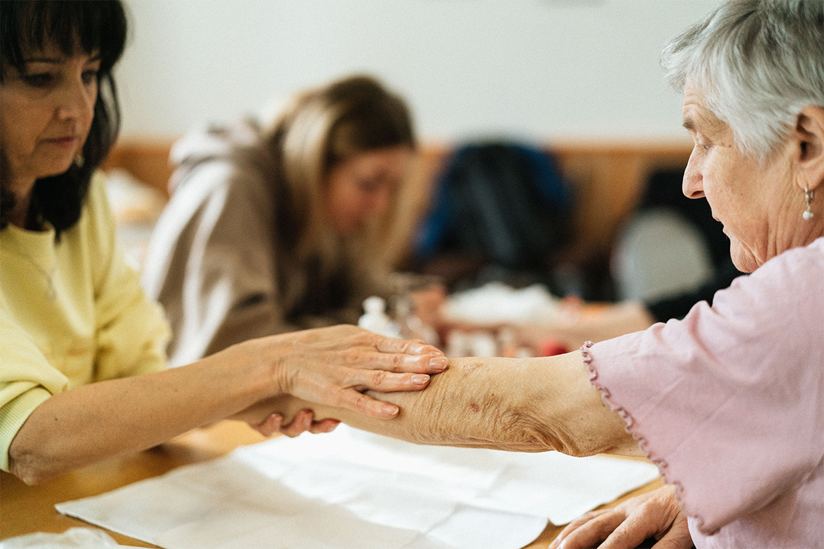 J&uuml;ngere Frau h&auml;lt f&uuml;rsorglich die Hand einer &auml;lteren Frau am Tisch
