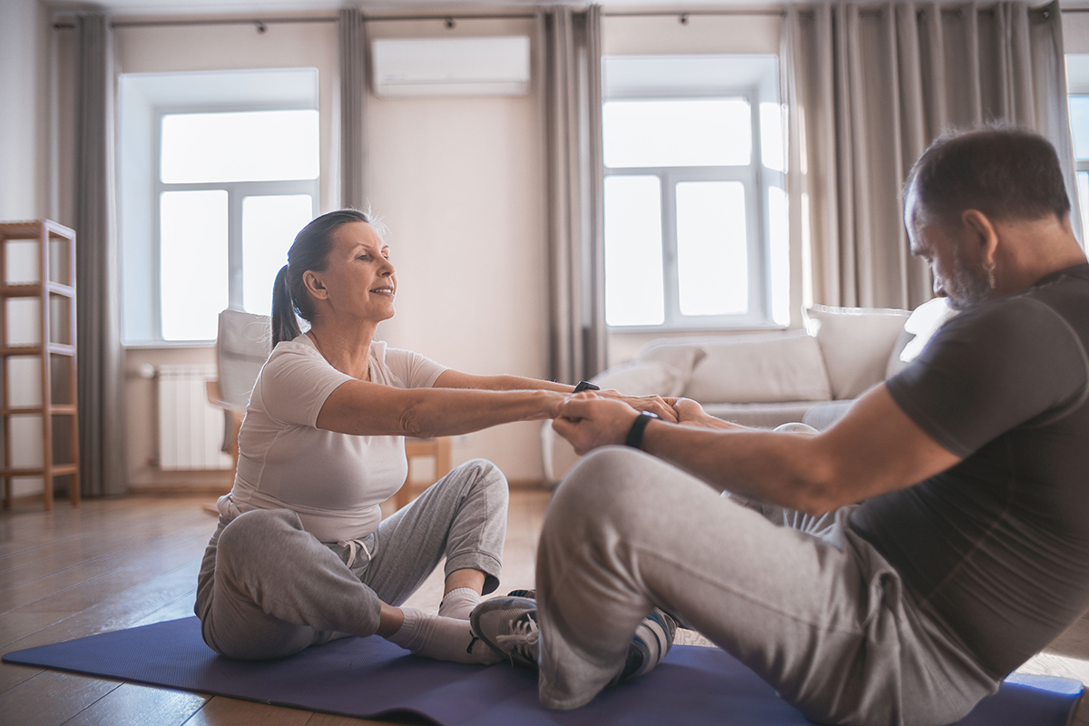 &Auml;lteres Paar macht gemeinsam Dehn&uuml;bungen auf einer Yogamatte im Wohnzimmer