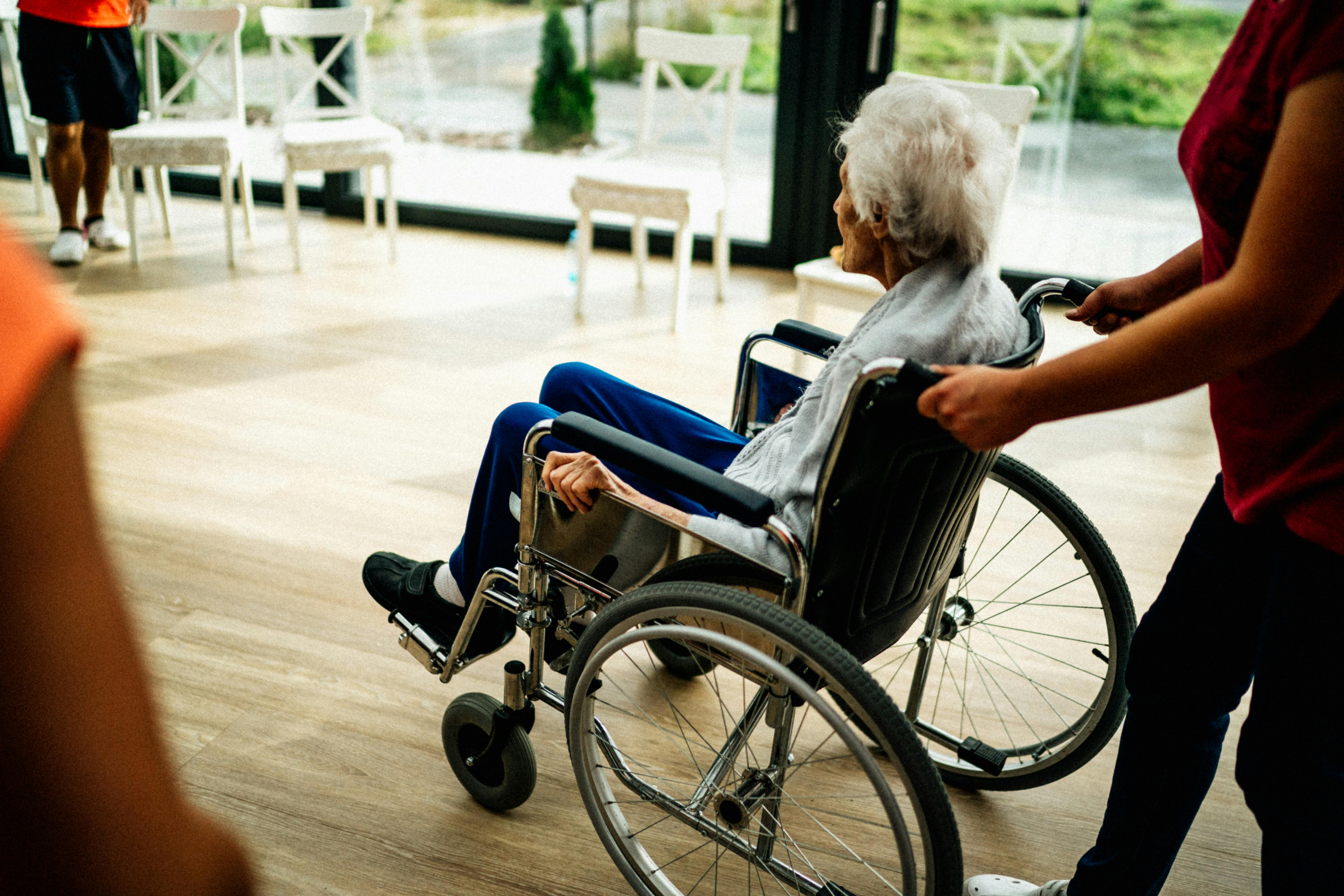Eine Pflegefachkraft schiebt eine ältere Frau im Rollstuhl.
