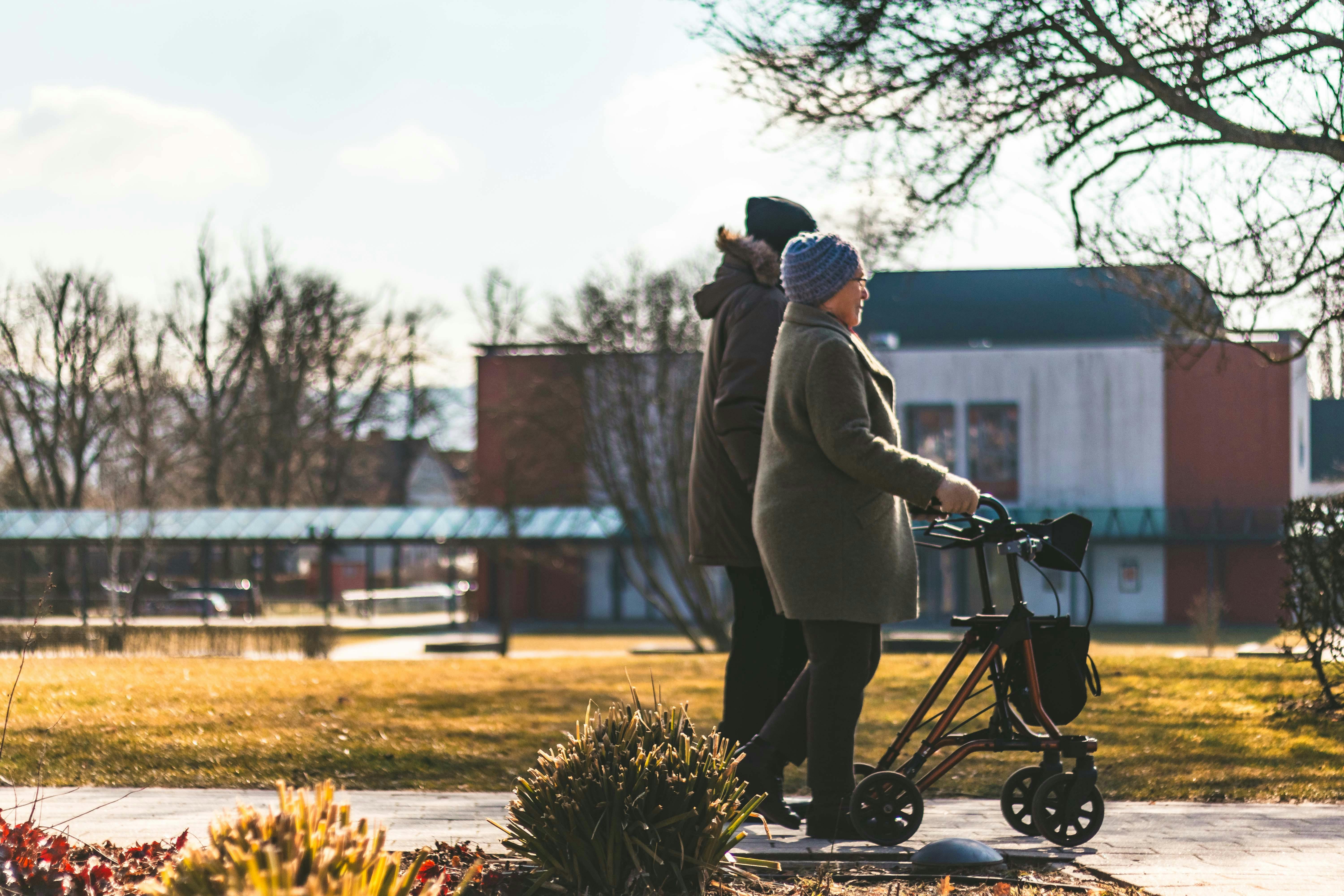 Ein junger Mann begleitet eine ältere Frau beim Spaziergang mit dem Rollator.