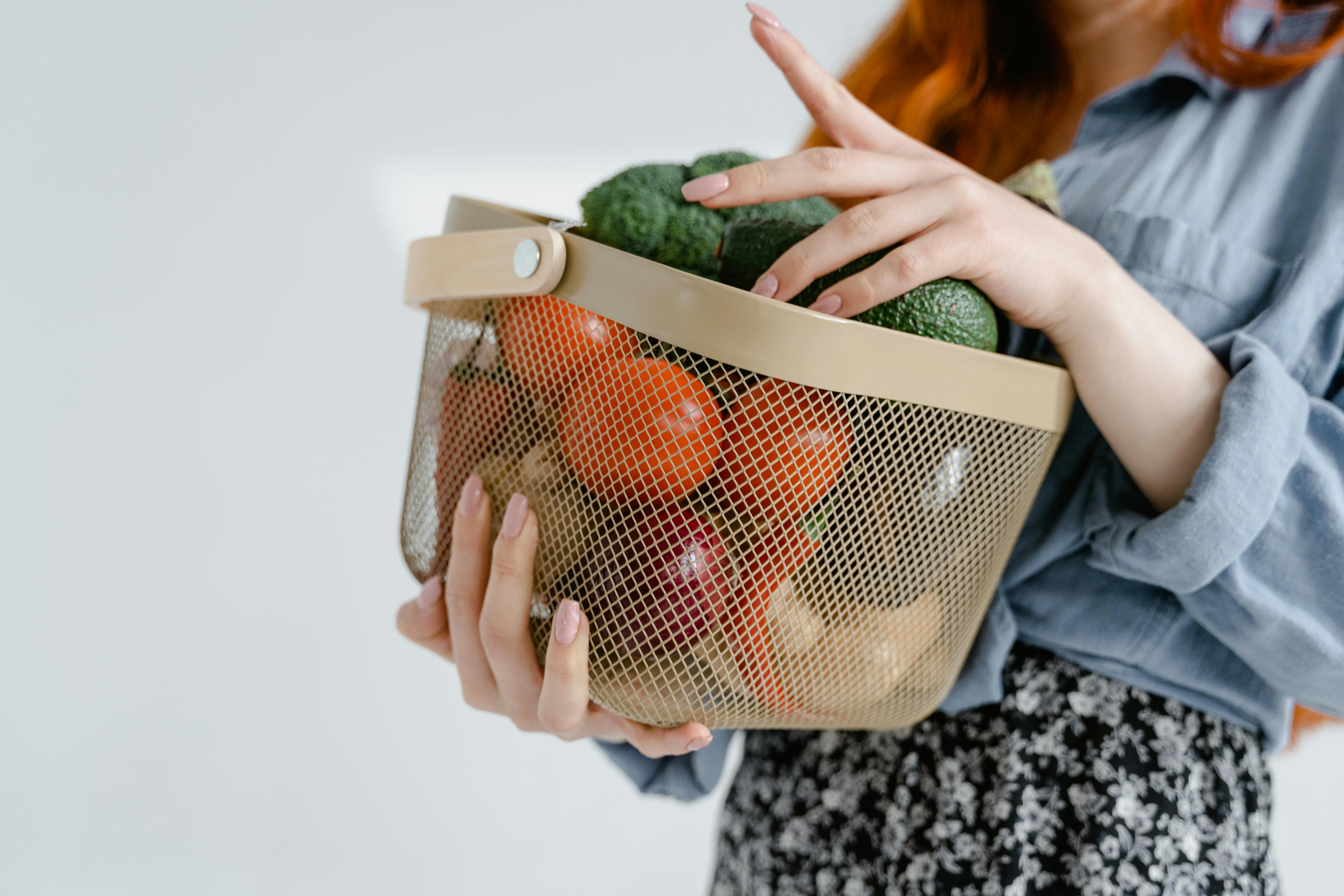 Eine Frau trägt einen Einkaufskorb mit Obst und Gemüse.
