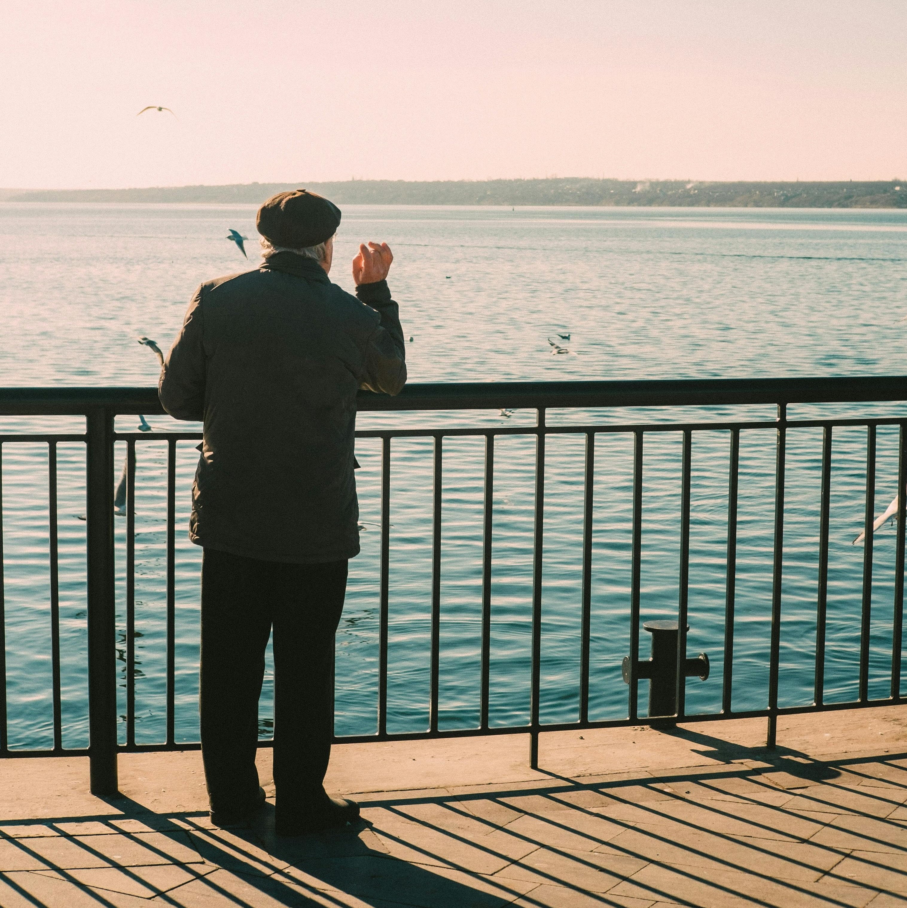 Ein älterer Mann steht am Geländer an einem See und blickt über das Wasser.