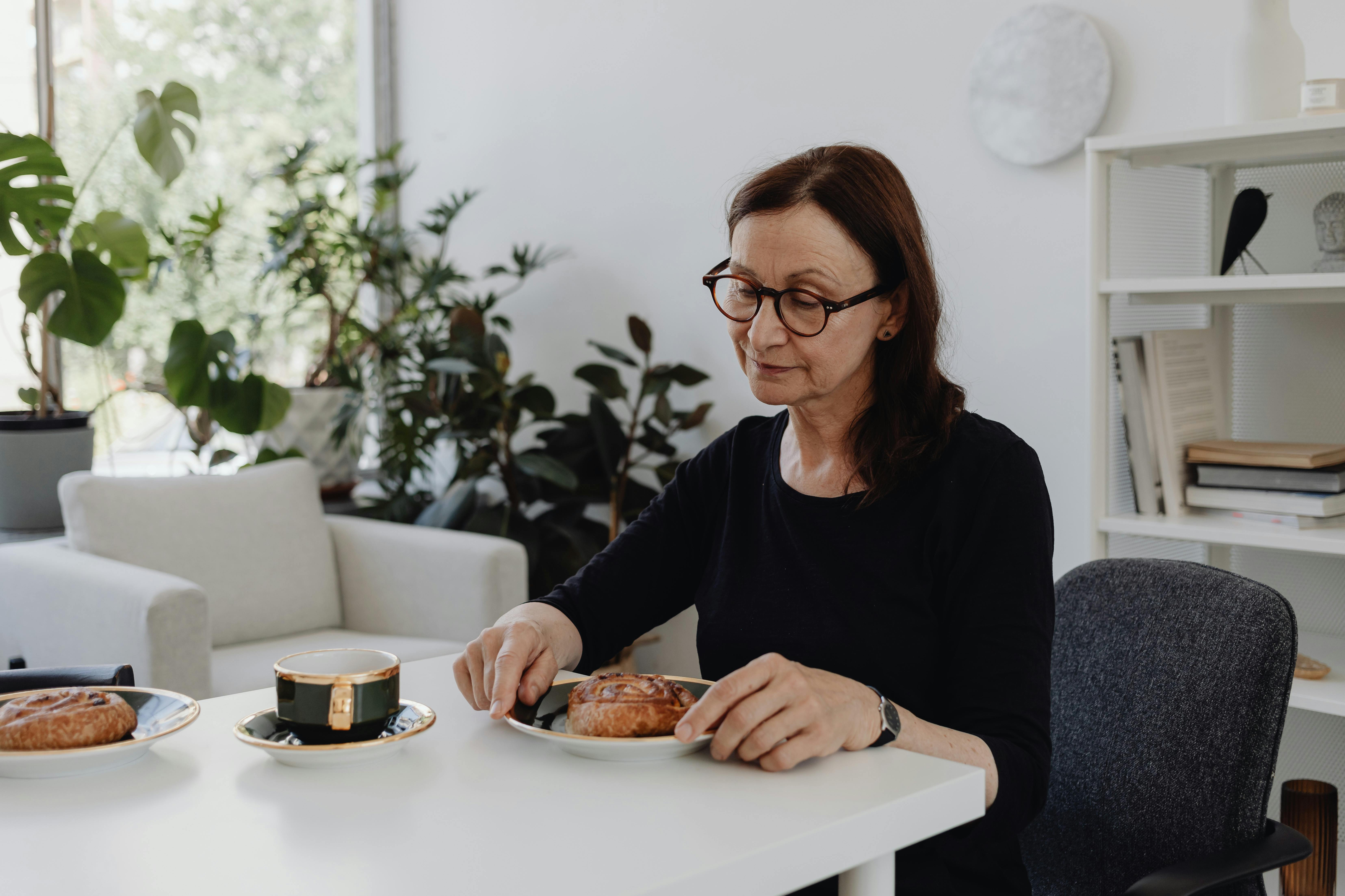 Eine Frau sitzt am Esstisch. Vor ihr steht Gebäck und Tee.