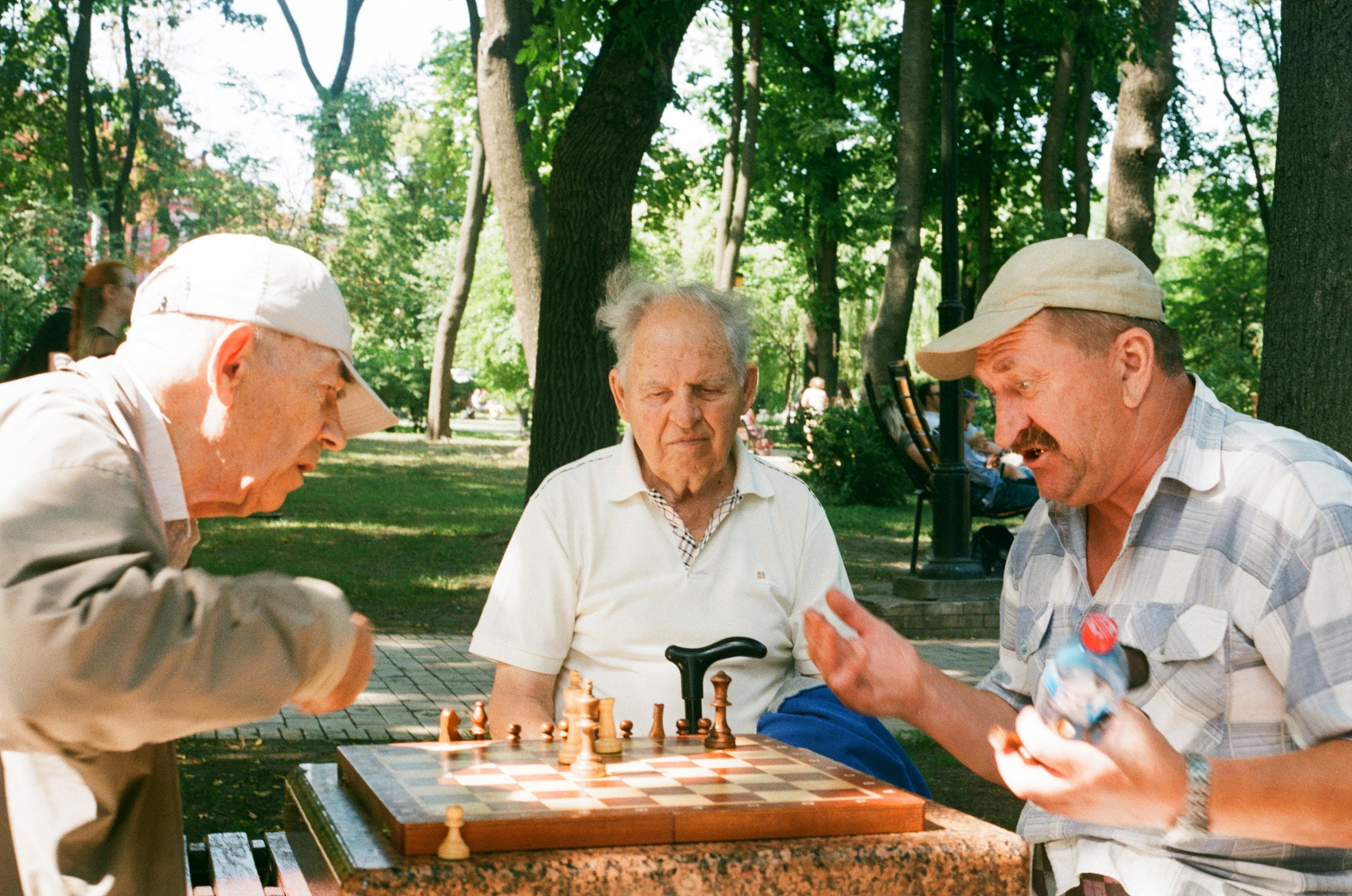 Drei &auml;ltere M&auml;nner spielen konzentriert Schach an einem Tisch im Park