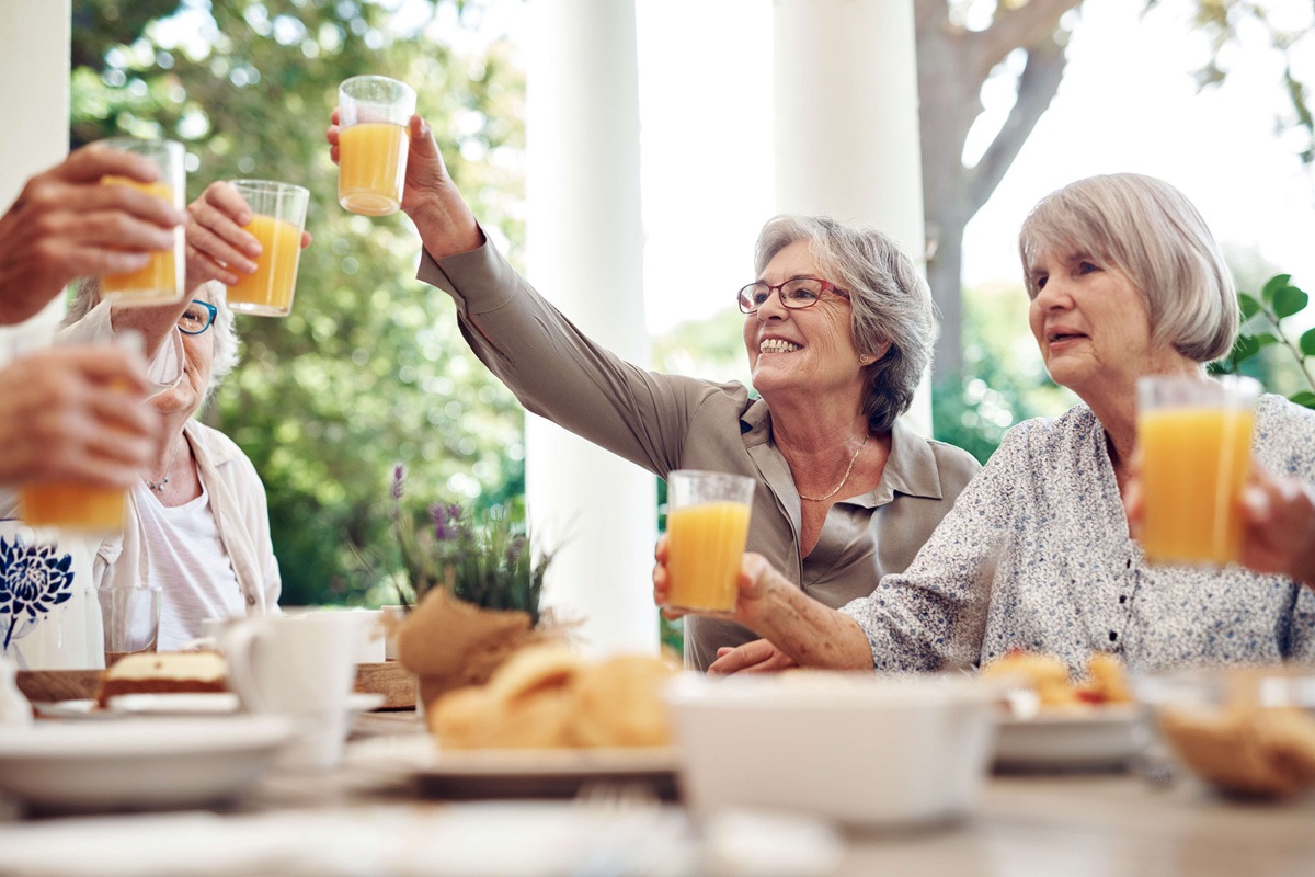 &Auml;ltere Frauen sto&szlig;en beim Fr&uuml;hst&uuml;ck im Freien fr&ouml;hlich mit Orangensaft an