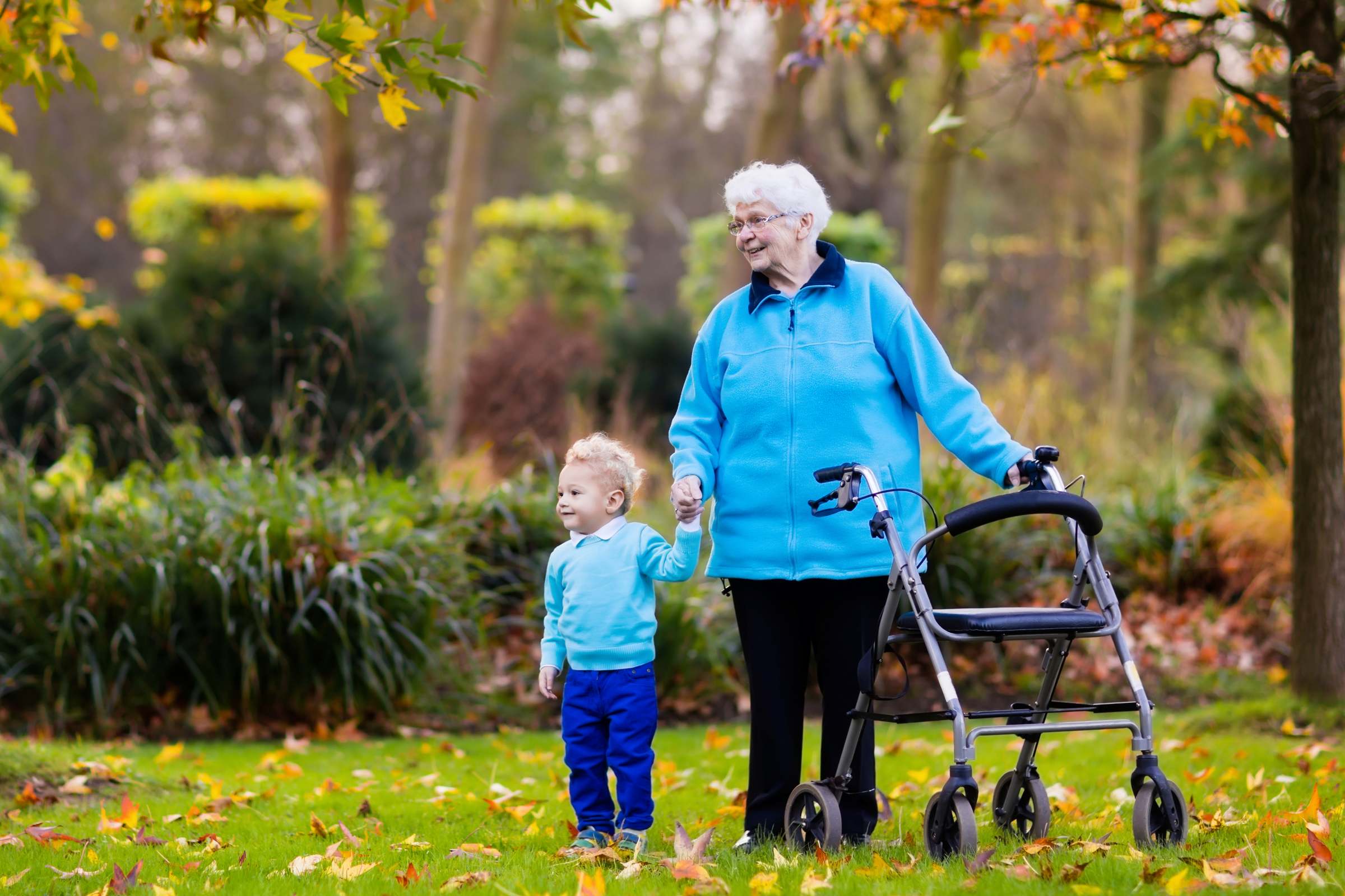 &Auml;ltere Frau mit Rollator geht im herbstlichen Park an der Hand eines kleinen Jungen