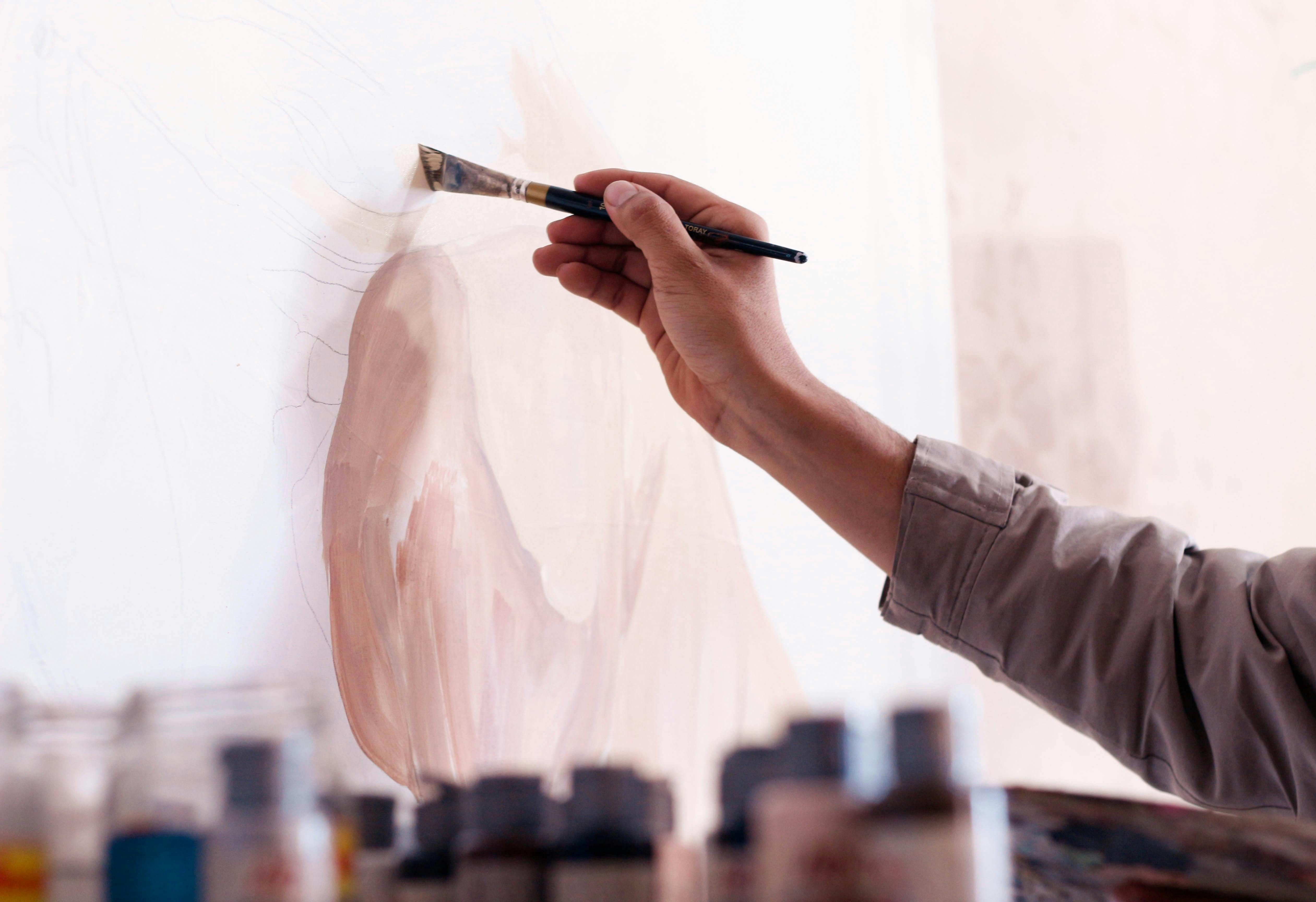 Hand malt mit Pinsel ein Portr&auml;t auf eine Leinwand, davor Farbt&ouml;pfe